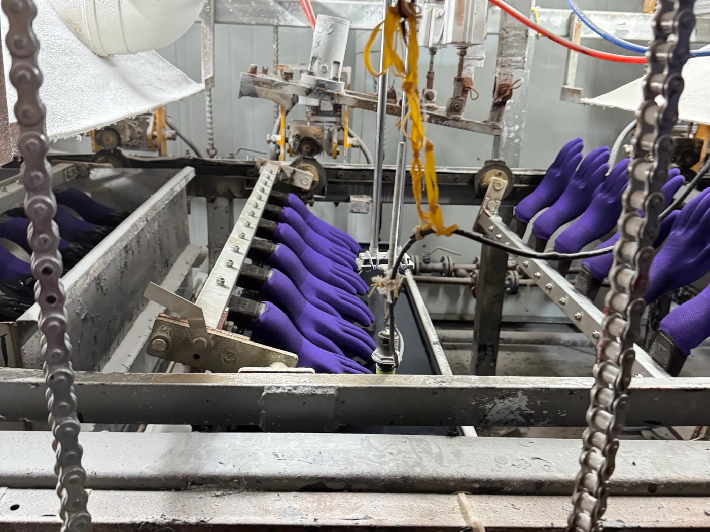 Línea de producción de guantes con recubrimiento de nitrilo visible sobre los moldes